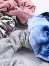Pack de cuatro coleros de pelo con diseños variados: uno rosa liso, uno plateado brillante, uno azul con efecto tie-dye y uno plateado con glitter.