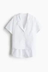 Conjunto de pijama corto blanco de algodón con broderie. Incluye una camisa de manga corta con cuello abierto, botones adelante, bolsillo superior abierto y bajo recto con aberturas laterales. El short tiene cintura elástica.