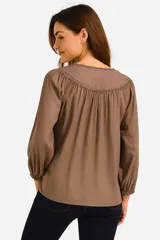 Camisa color crema con cuello a la base, mangas largas abullonadas con puños elásticos, escote en V con cordones y borlas.