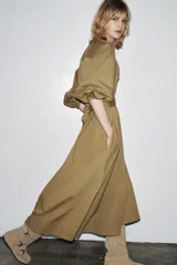Bota alta color beige de serraje con puntera redondeada. Presenta tres tiras con hebillas metálicas en la parte delantera y caña.