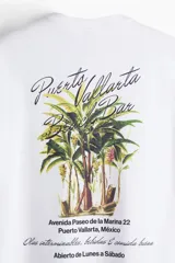 Remera blanca de algodón con cuello redondo y hombros caídos. Estampado pequeño en el pecho con la frase "Puerto Vallarta Beach Bar". Corte holgado.