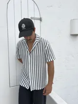 Camisa tejida a rayas verticales blancas y negras, de manga corta y cuello solapa.