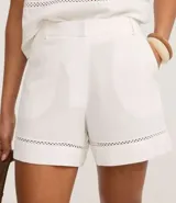 Short femenino confeccionado en viscolino de color blanco, con cierre tradicional, trabillas en la cintura y bolsillos. Presenta un detalle decorativo de entremeio calado en el bajo.