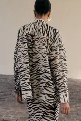 Camisa de manga larga con estampado de cebra en tonos blanco y negro. Tiene cuello clásico, cierre frontal con botones y un bolsillo de parche en el pecho.
