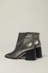 Botín de cuero metalizado color peltre con punta fina y cierre lateral. Tiene taco geométrico de madera color negro.