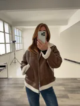 Campera marrón de cuero sintético con interior de piel sintética color crema, cierre frontal con cremallera y hebillas ajustables en el cuello y la cintura.
