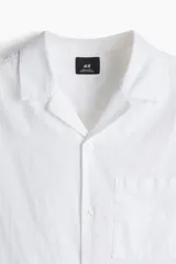 Camisa blanca de manga corta en mezcla de algodón y lino. Modelo con cuello abierto, tapeta lisa y bolsillo superior abierto.
