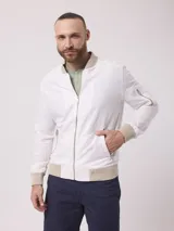 Campera bomber color blanco confeccionada en lino y algodón, con cuello mao, cierre frontal con cremallera, bolsillos frontales con cierre y puños y ruedo acanalados en color beige.