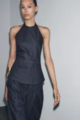 Top de cuello halter confeccionado en tejido denim azul. Detalle de pespuntes marcados a tono y espalda descubierta.