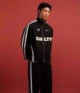 Campera deportiva negra con cuello alto y cierre frontal. Presenta franjas blancas contrastantes a lo largo de las mangas y detalles gráficos en blanco en el pecho, incluyendo la palabra "GUILTY" en grande.