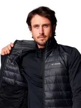 Chaqueta híbrida Columbia para hombre, color negro. Presenta un cuerpo acolchado con aislamiento Thermator reciclado y mangas de tejido softshell elástico y transpirable. Tiene cuello alto, cierre frontal completo y bolsillos laterales con cremallera.