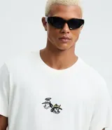 Remera blanca de algodón con cuello redondo y mangas cortas. Presenta un estampado estilo grafiti en la espalda con lettering en amarillo y rosa, y la ilustración de un perro con gorra y aerosol.