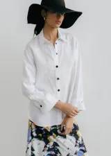 Camisa blanca de lino con cuello clásico, manga larga con puños abotonados y abertura en los laterales.