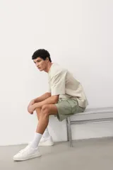Short cargo color verde claro en popelina de algodón, con cintura elástica ajustable con cordón, bolsillos laterales, bolsillos cargo con solapa y botón a presión en piernas y traseros, y aberturas laterales en el bajo.
