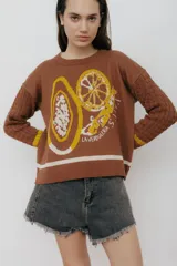 Sweater marrón de punto con diseño jacquard de frutas y verduras en amarillo y blanco. Tiene mangas tejidas en ochos, bordado en la espalda y puños con agujeros para los dedos.