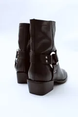 Bota de cuero negra con caña media, puntera ligeramente afilada y detalle de correa con herraje metálico circular y tachas. Taco bajo y ancho.