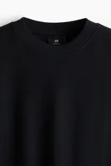 Remera negra de punto de algodón pesado, corte oversized, con cuello redondo ribeteado, hombros caídos y bajo recto.