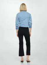 Pantalón de jean negro de corte cropped y acampanado, con tiro alto, cinco bolsillos y ruedo desflecado.