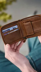 Billetera de cuero marrón con doble pespunte artesanal y cierre perimetral. El interior cuenta con compartimentos para billetes, tarjeteros y un monedero con broche.