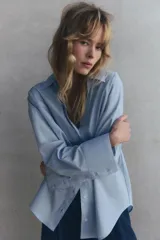 Camisa celeste de popelina de algodón, con cuello solapa, escote pico, manga larga con puños y cierre frontal con botones.