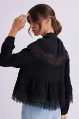 Blusa negra con cuello alto y mangas largas, con detalles de encaje en el pecho, mangas y ruedo.