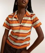 Blusa femenina de punto con cuello polo, mangas cortas y estampado de rayas horizontales en tonos naranja, marrón, blanco y verde.