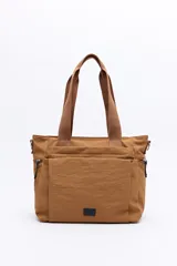 Cartera de nylon color marrón, con asas superiores reforzadas y correa larga regulable y desmontable. Cuenta con bolsillos frontales y laterales con cierre metálico, y un parche con el logo de la marca en la parte inferior delantera.