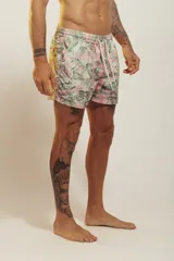 Short de baño para hombre, tiro medio, con estampado tropical en tonos rosados, verdes y blancos. Posee cintura elástica con cordón de ajuste trenzado y bolsillos laterales.
