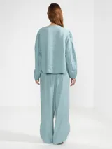 Camisa de lino color blanco, con cuello en V, manga larga con puños elásticos, cierre frontal con botones y dobladillo curvado.