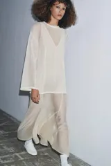 Vestido largo de punto ligero color crudo, con cuello redondo y mangas largas. Presenta un forro interior de tela satinada color beige claro que asoma en el bajo, creando un efecto de dos piezas.