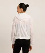 Campera rompevientos deportiva blanca, confeccionada en poliamida, con capucha, cierre delantero en cremallera, tirador gomoso y puños ajustados.