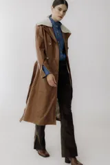 Trench de cuero color camel con cuello de piel sintética color crema, doble botonadura, bolsillos laterales y corte evasé.