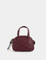 Cartera bowling color borgoña de cuerina con doble asa corta de mano, correa regulable y cierre superior. Incluye charm lateral.