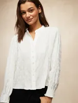 Camisa blanca de manga larga con textura arrugada, cuello mao y puños elásticos.