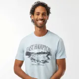 Camiseta celeste de manga corta con cuello redondo. Estampado frontal con el texto "East Hampton New York - United States" y un dibujo de un yate.
