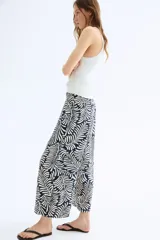 Pantalón tobillero cropped de viscosa con estampado de hojas en color crema sobre fondo azul marino. Tiene tiro alto con elástico en la cintura, bolsillos laterales y piernas amplias rectas.