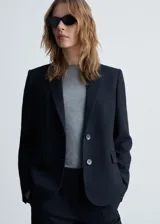 Blazer negro con raya diplomática, cuello de pico con solapa, cierre de botones en la parte delantera, manga larga con puños abotonados, diseño recto y estructurado, un bolsillo de ribete en el pecho y dos bolsillos de ribete con solapa laterales.