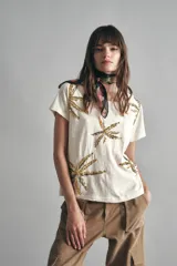 Remera de mangas cortas color crudo, de calce relajado y escote redondo. El frente se encuentra bordado con un diseño de palmeras en lentejuelas y canutillos.