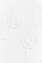 Camiseta blanca de cuello redondo y manga corta con detalle de flores con volumen en delantero a tono.