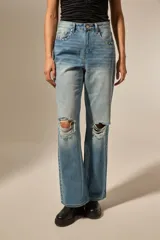 Pantalón jean azul claro, de corte recto, con roturas en las rodillas y detalles de tachas metálicas en los laterales y bolsillos.