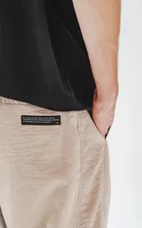 Pantalón beige de corte sastrero con bolsillos laterales, estilo holgado y tela suede. Cintura trasera con doble ajuste elástico y tanca, cintura delantera con botón y cierre.