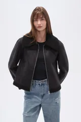 Campera negra de estilo aviador, confeccionada en material tipo gamuza o suede, con cuello y forro de corderito (shearling) negro. Presenta cierre frontal metálico y puños y ruedo con terminación de corderito.