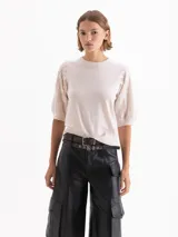 Top color beige de largo a la primera cadera, con mangas bombachas decoradas con flecos, confeccionado en una mezcla de hilados.