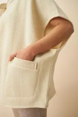 Chaleco color crema de lana sin teñir, corte recto, con cuello y solapa pronunciadas, broches a presión y bolsillos ojal.