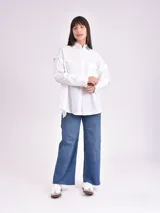 Camisa celeste de corte amplio, con cuello clásico, cierre frontal con botones, bolsillo en el pecho y mangas largas con detalle de botones en los puños.