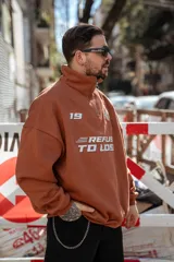 Buzo marrón con cierre medio, cuello alto y corte oversize. Estampado frontal con el número 19, un ancla con laureles y la frase "Refuse to Lose".