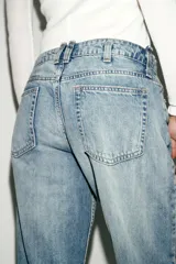 Jeans de tiro bajo, corte recto y pierna ancha, color celeste claro desgastado. Presenta roturas visibles en la zona de la rodilla y pequeños desgastes en los muslos y bolsillos.