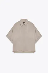 Camisa color beige de corte holgado, con cuello solapa, manga corta con dobladillo y dos bolsillos de parche en el pecho.