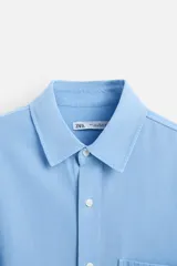 Camisa celeste de lyocell y algodón, corte relaxed fit, cuello solapa, manga larga con puños abotonados, bolsillo de parche en el pecho y cierre frontal con botones.
