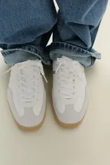 Zapatillas deportivas blancas con detalles plateados y suela color caramelo.
